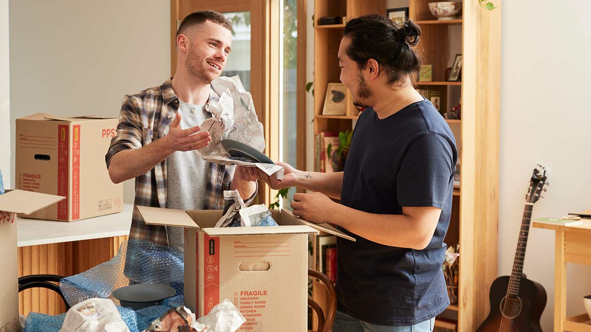 Two young men unpacking household items from boxes in living room