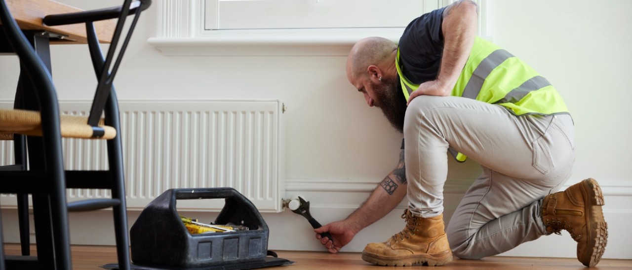 A tradesperson in a hi vis vest adjusts a hydronic heater with a wrench