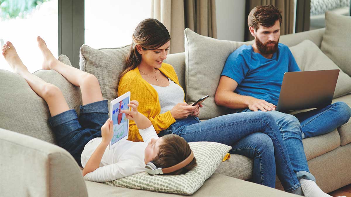Parents and child on couch using electronic devices