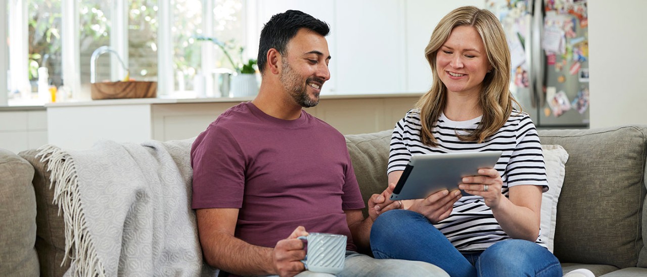 Couple sitting on couch looking at tablet.