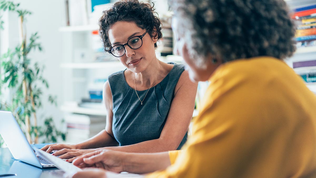 Woman working on computer while consulting female client