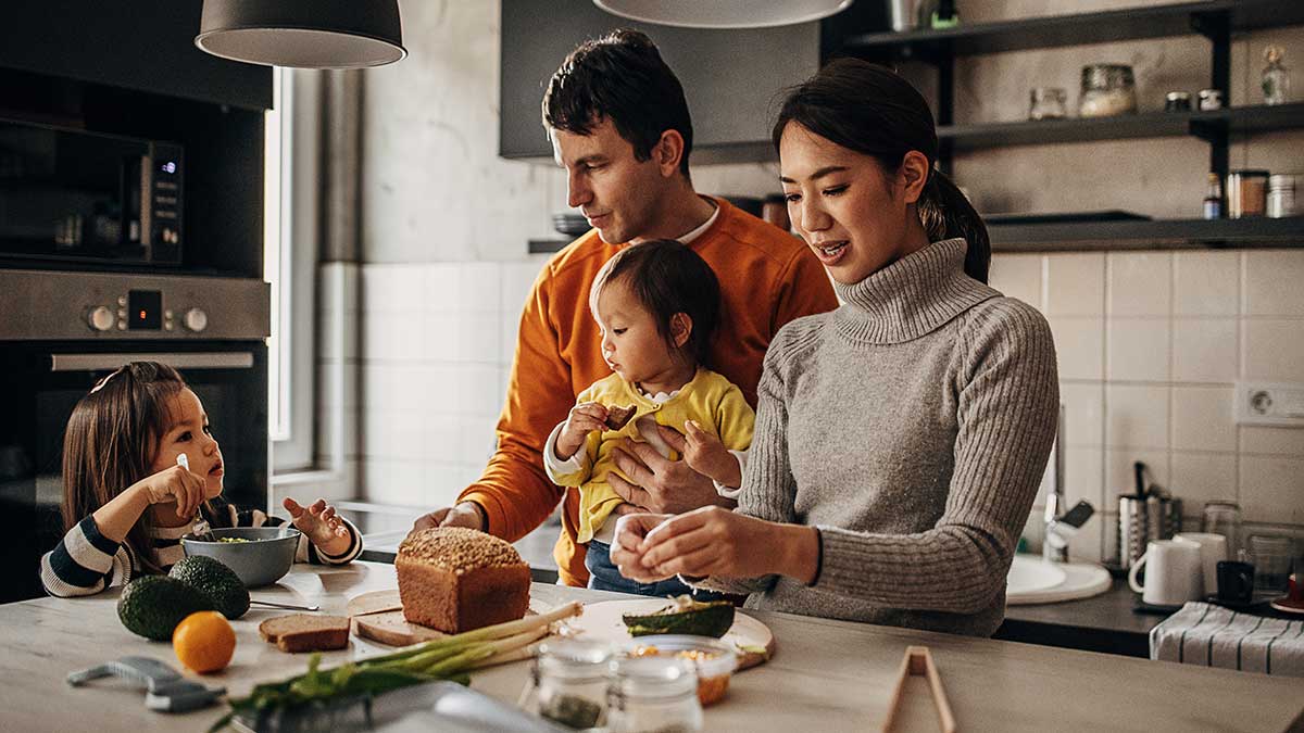 Parents and two young children in kitchen preparing meal.