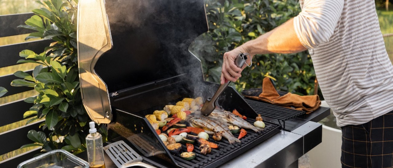 A person cooking an assortment of meat, fish and vegetables on a gas barbecue