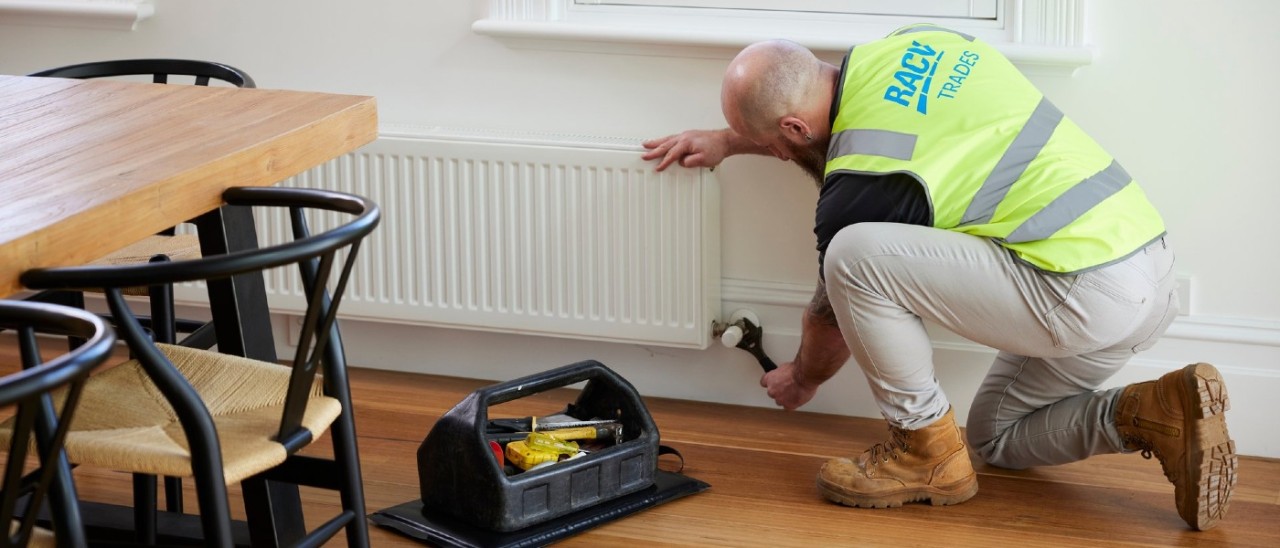 A technician wearing an RACV-branded safety vest adjusts a hydronic heater