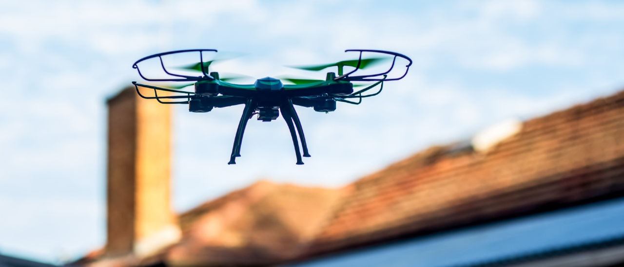 drone in flight with suburban home roof in background