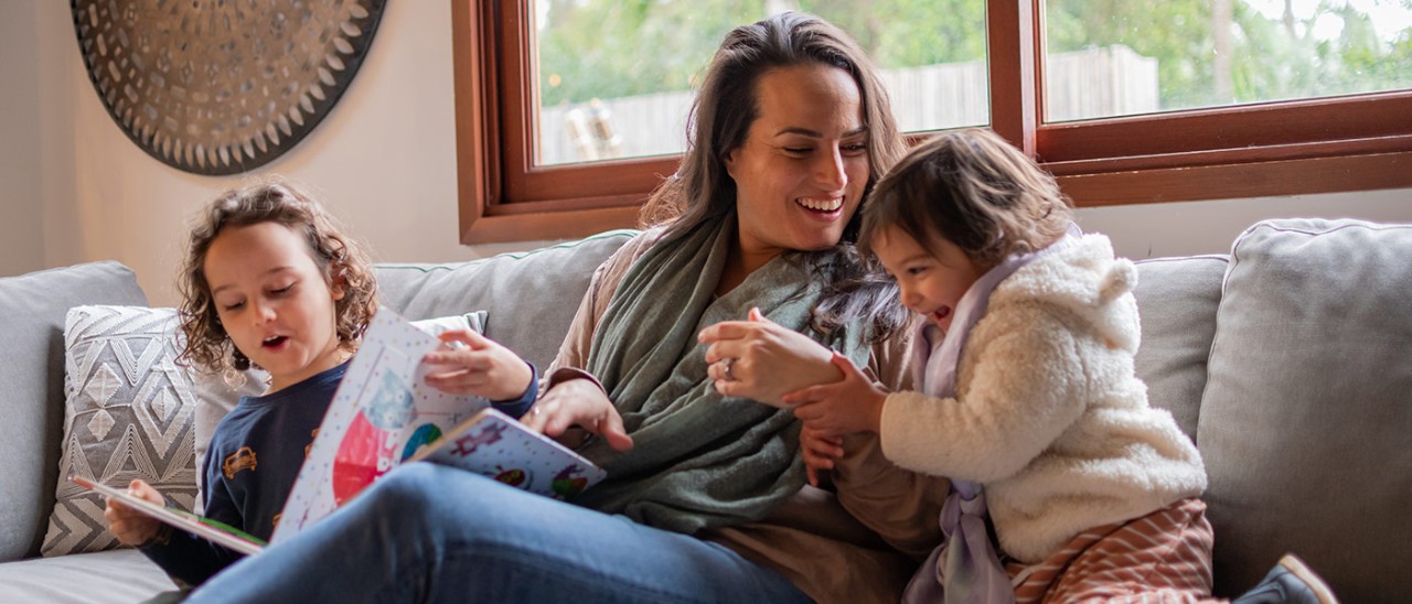 Mother on couch with two young children laughing and reading books.