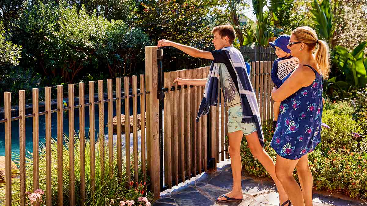 Boy opening pool safety gate for mother and toddler