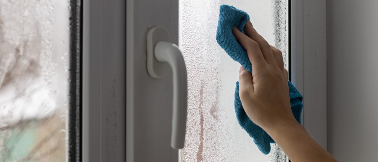 A hand using a blue cloth to clean a window covered in condensation