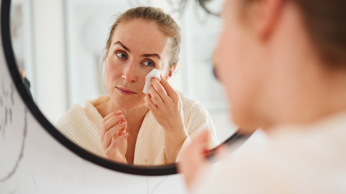 A woman wiping her face with a tissue in a mirror