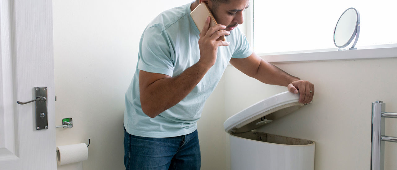 A man calling someone on a mobile phone while her examines the cistern on a toilet