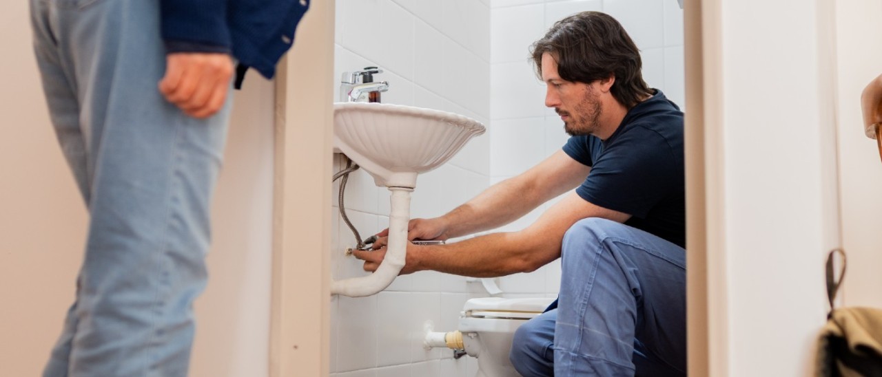 man fixing a sink flexi-hose while woman watches