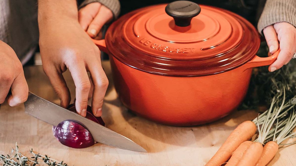 person cutting onion next to a soup pot and other ingredients
