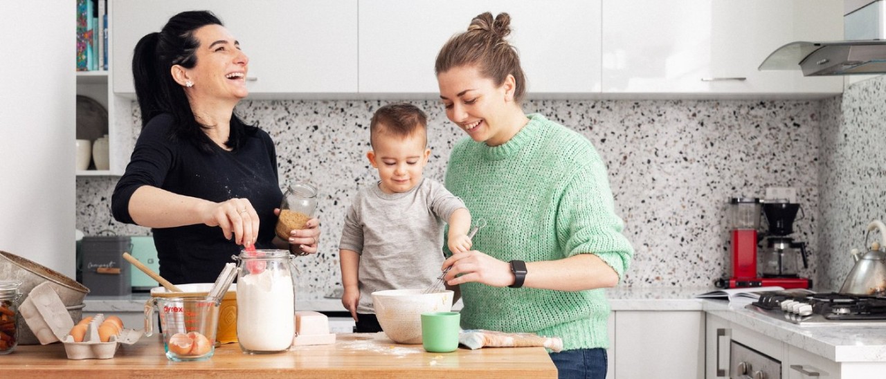 A couple smile and laugh in their modern kitchen while cooking something with their toddler A couple smile and laugh in their modern kitchen while cooking something with their toddler