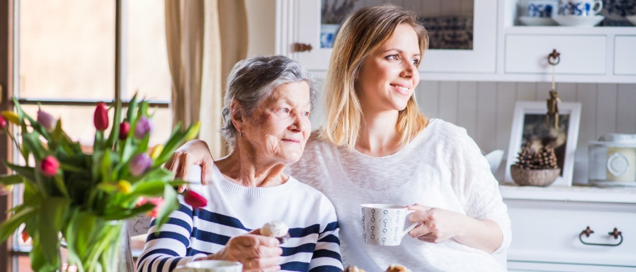adult woman and her elderly mother sitting drinking tea together