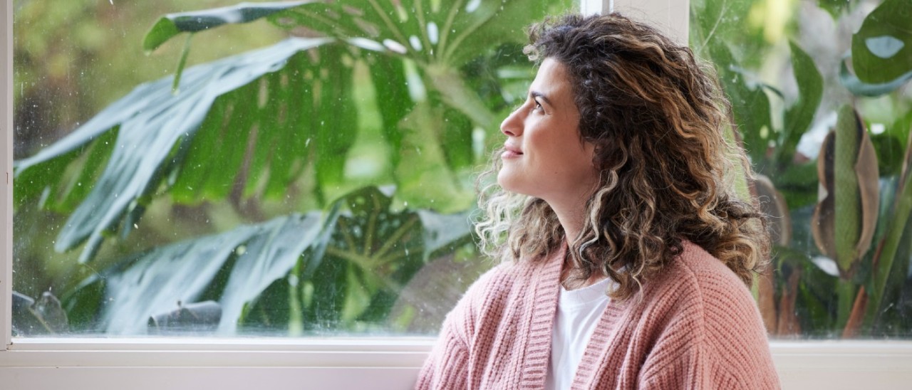 woman in pink cardigan holding a magazine and looking out a window
