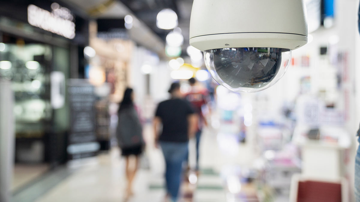 Shopping centre with close-up of security camera and blurred figures of people walking behind