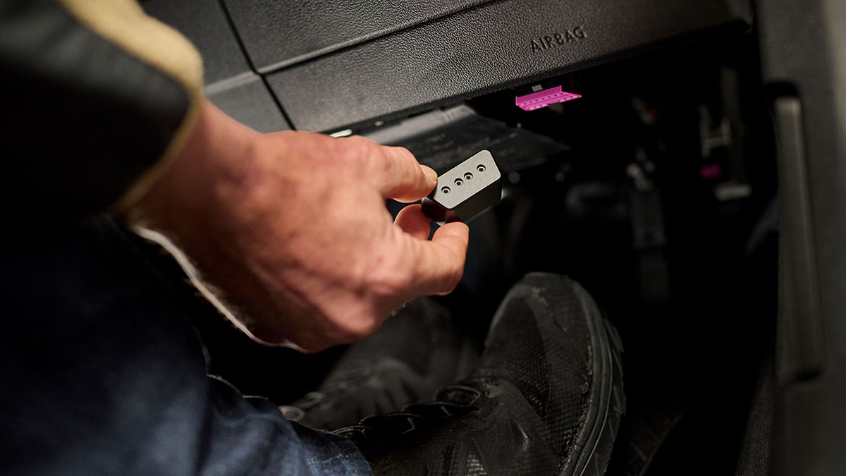 A close-up of a hand holding an OBD (On-Board Diagnostics) port inside a car.