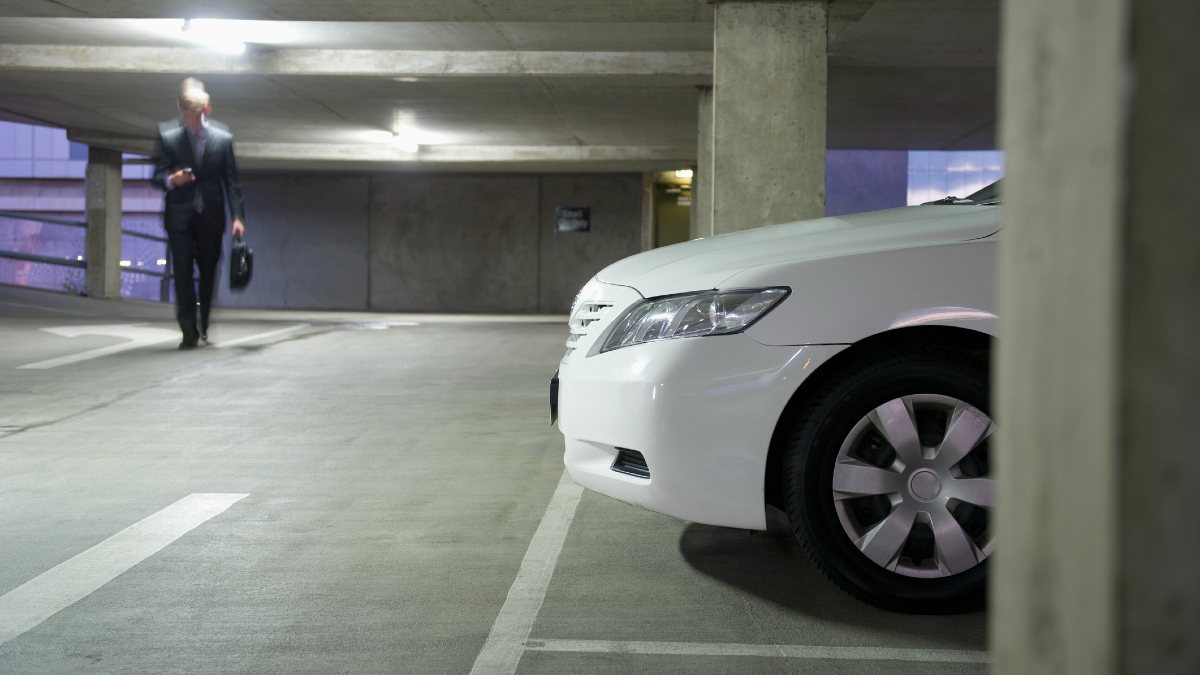 A man in a suit walking towards a white sedan in an underground car park