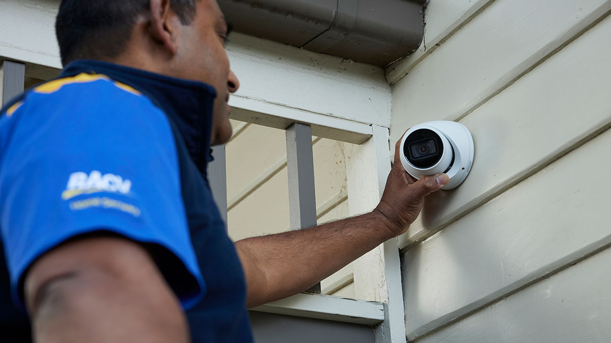 RACV security technician installing CCTV camera on outside of house