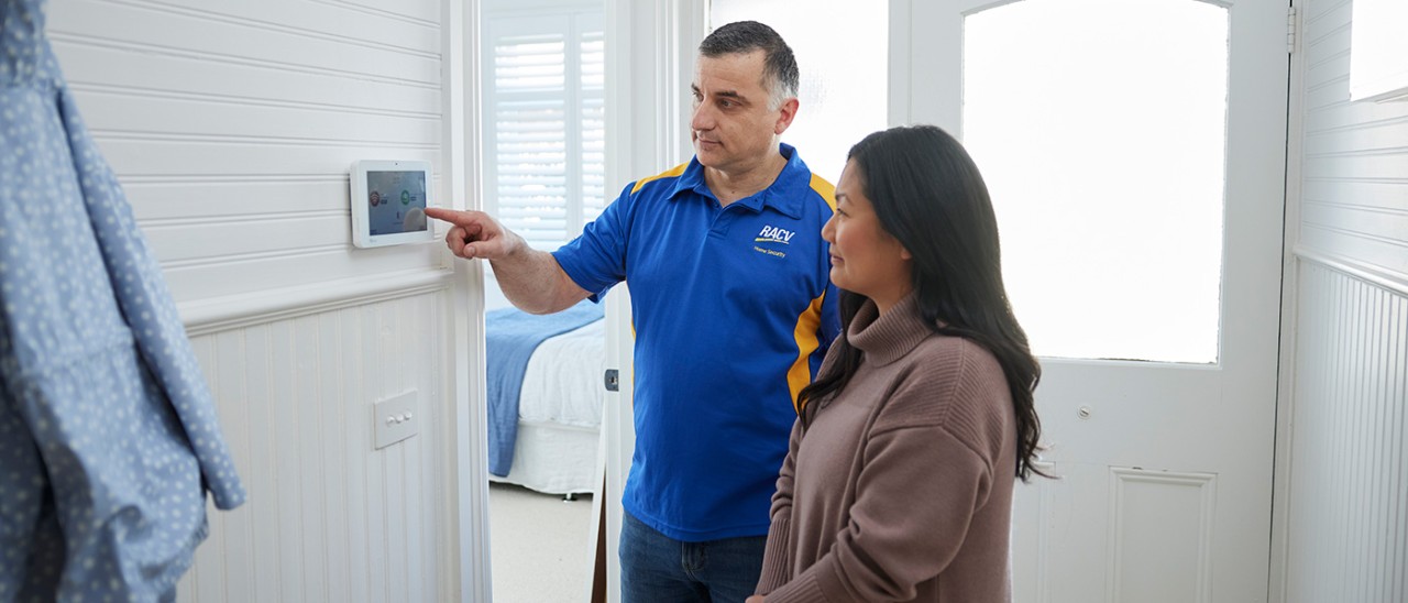 RACV-Home-Security-Alarm-Installation-1400x600 RACV security technician showing female customer the alarm panel in home