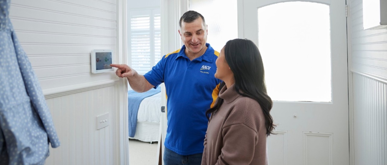 A home security technician showing a woman how her new in-home security system works via the panel inside the house