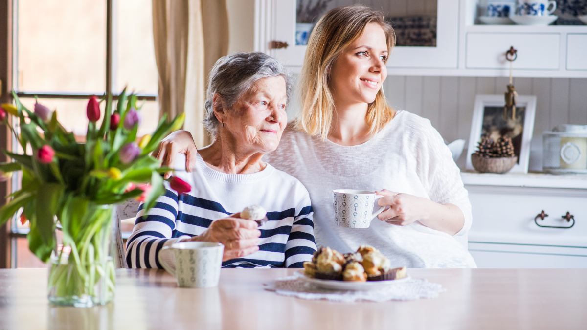 adult woman and her elderly mother sitting drinking tea together
