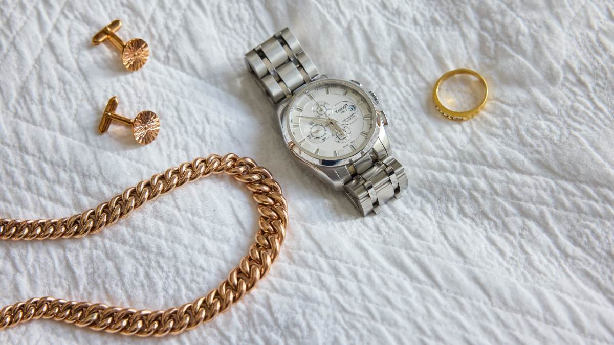 A gold chain, earrings, ring plus a silver watch laid out on a white cloth