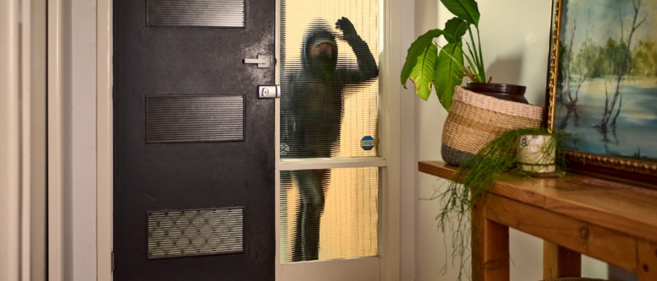 burglar in dark clothes and mask looking through front window into house