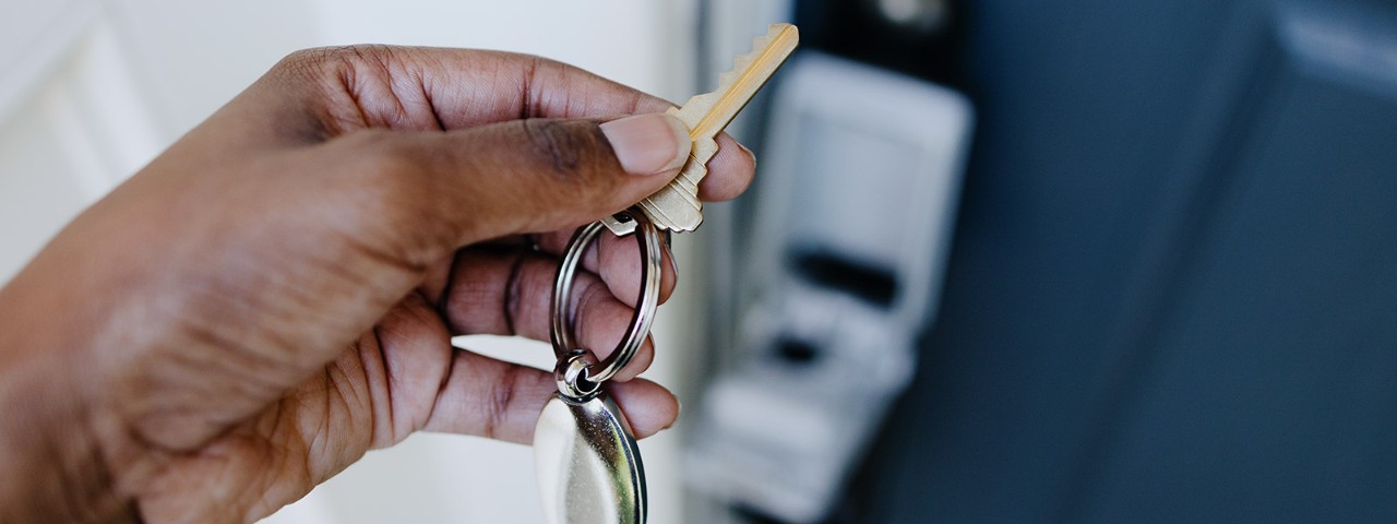 1417037963 hand with key and key safe attached to door behind