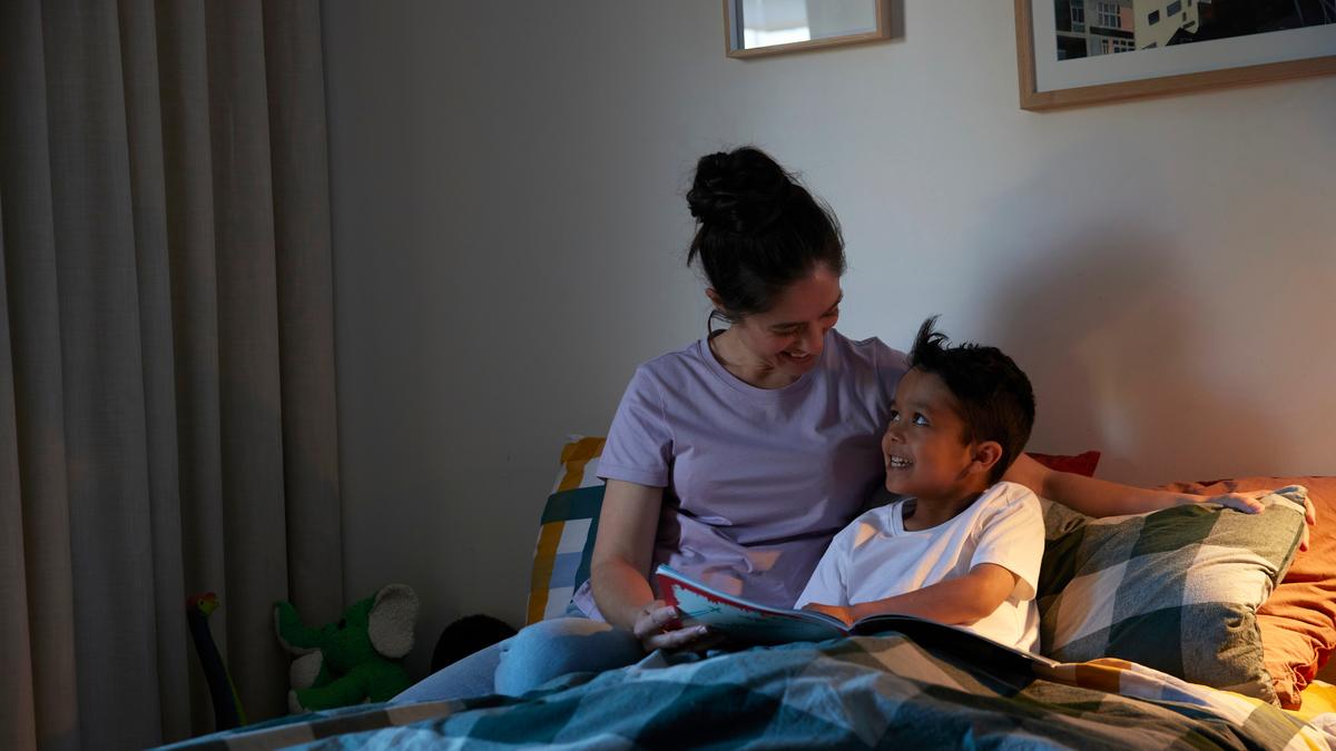 A mother reading a book to her school-age son in bed at nighttime