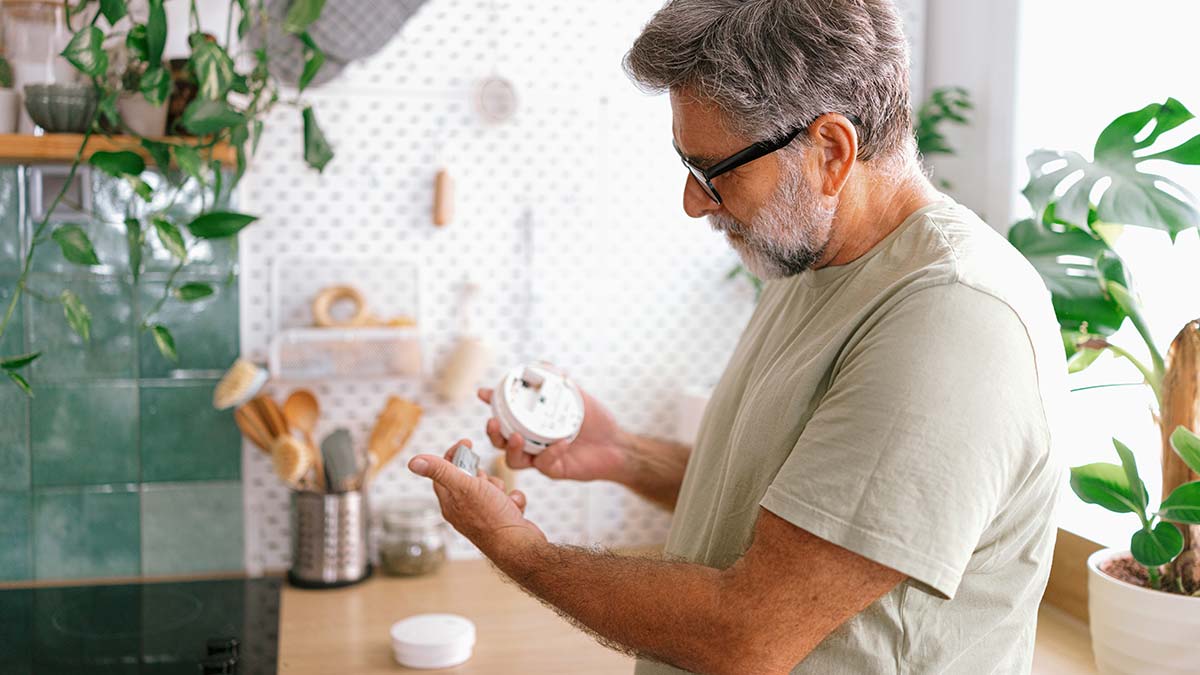 Man checks battery for smoke alarm in kitchen.