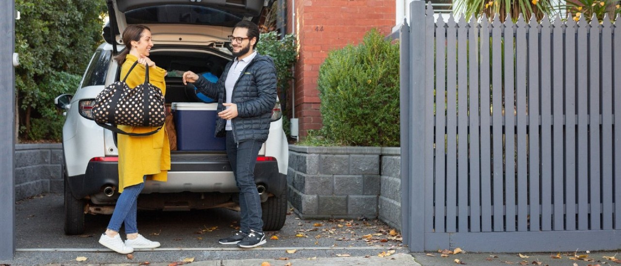 A woman and man happily taking luggage out of a SUV parked in a suburban driveway
