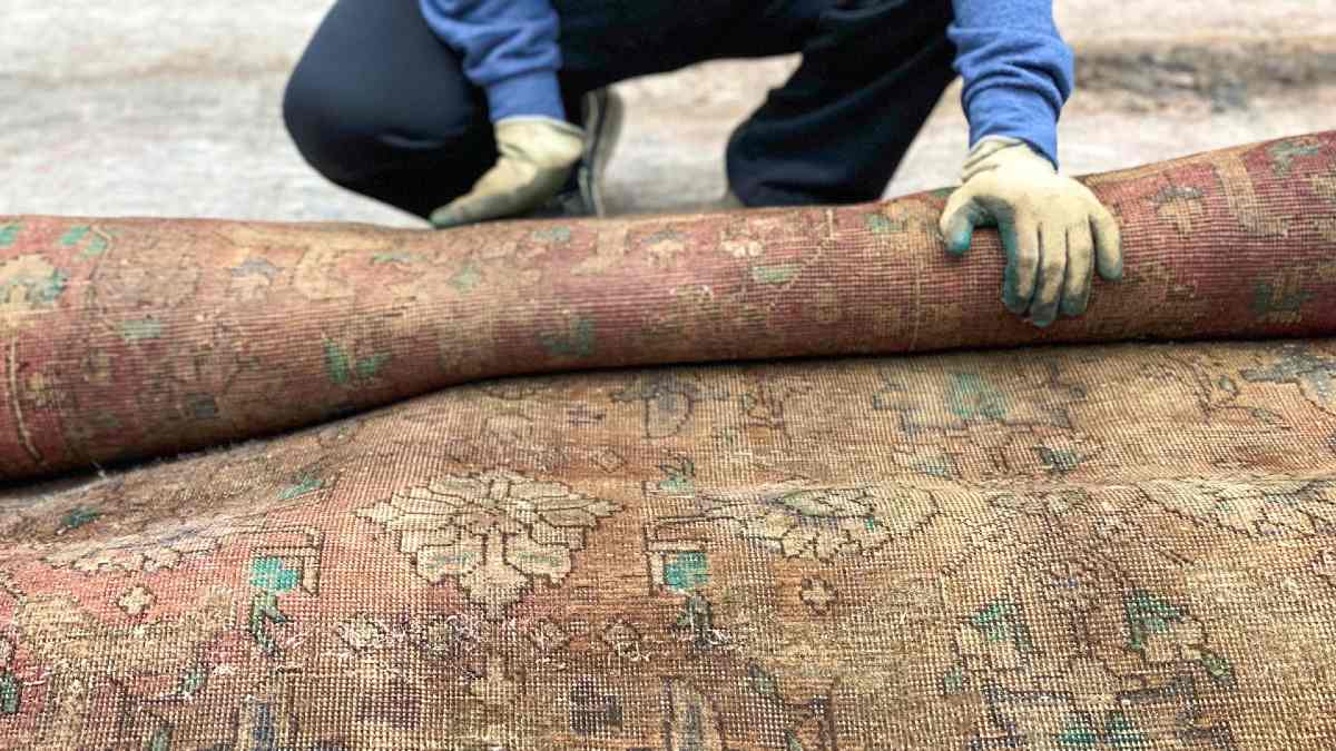 gloved man rolling up wet, dirty carpet