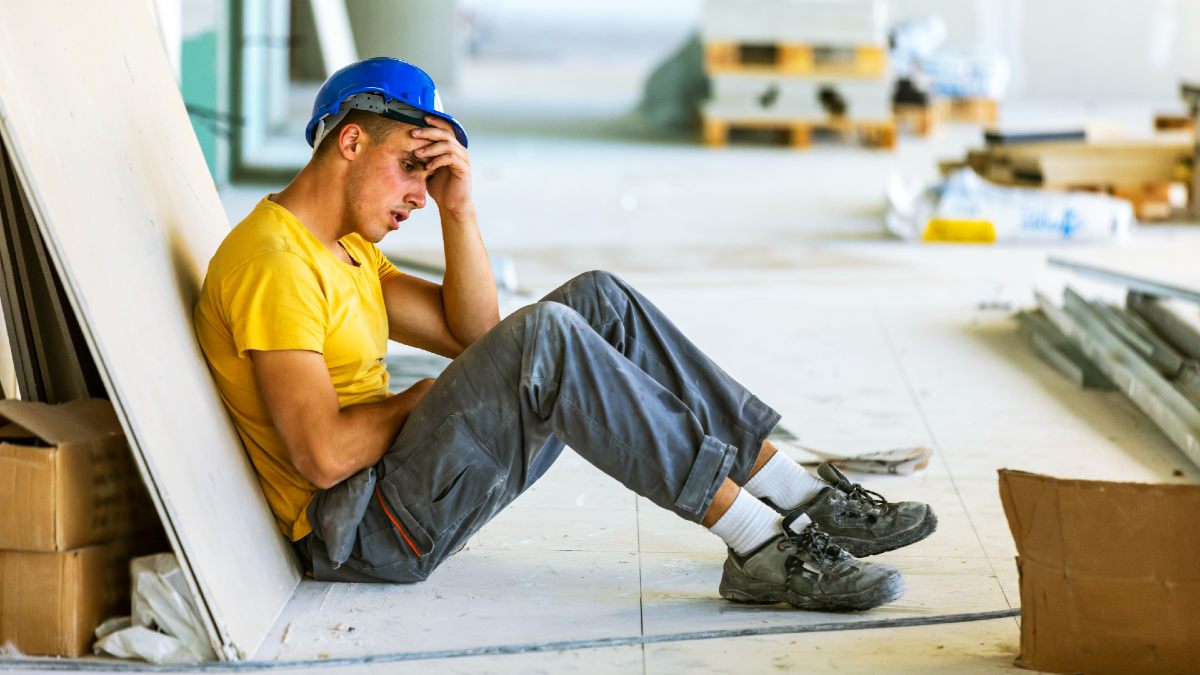 upset looking male tradie sitting slumped on the ground wearing a hard hat