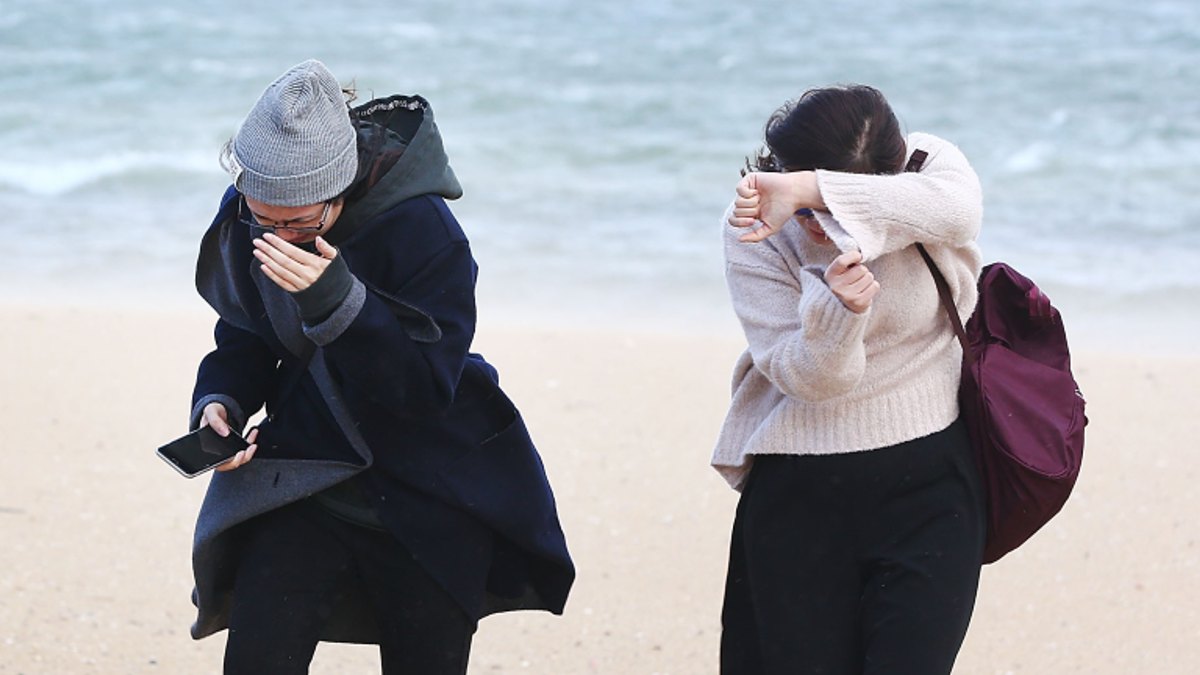 Two women shielding themselves from the wind on a beach