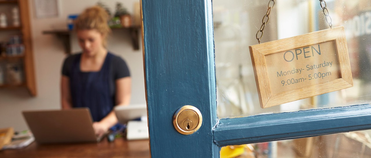 Close-up of shop door with retail worker in the distance working on computer.