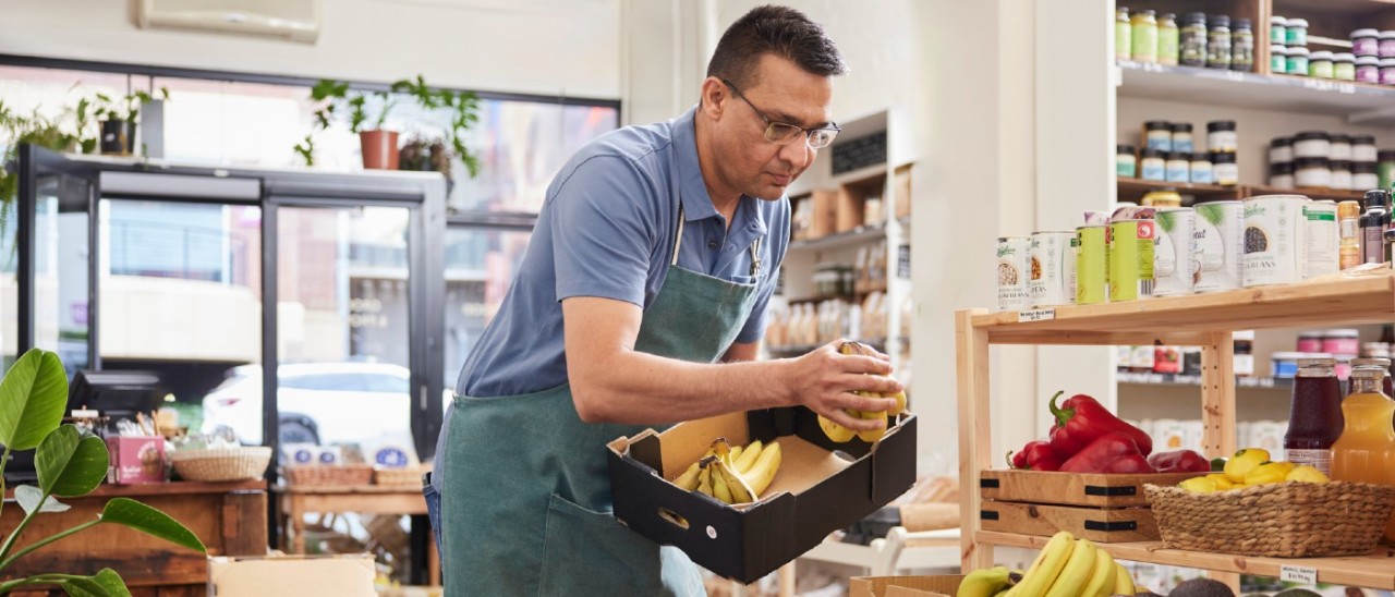 Grocery Retail Store_RACV Business Insurance man in apron stocking grocer shelves with fruit