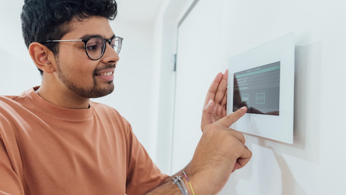 A young man using a smart home device mounted on a wall