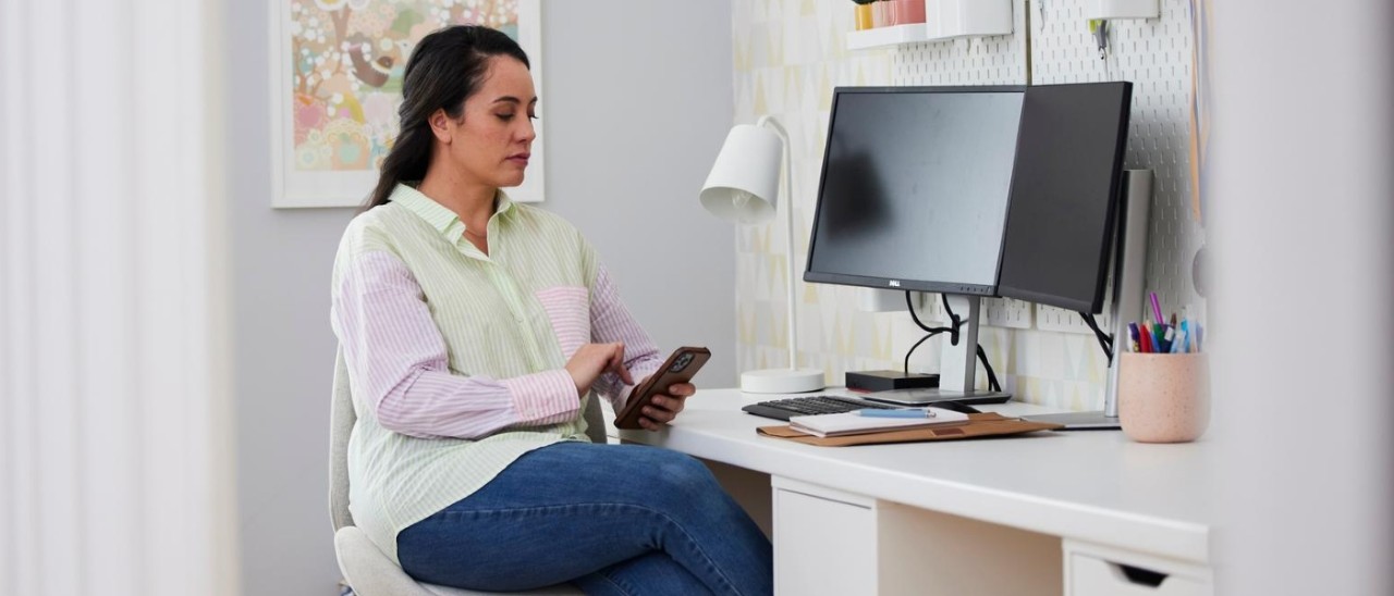 Woman in study A woman on her phone in front of a desktop computer at home
