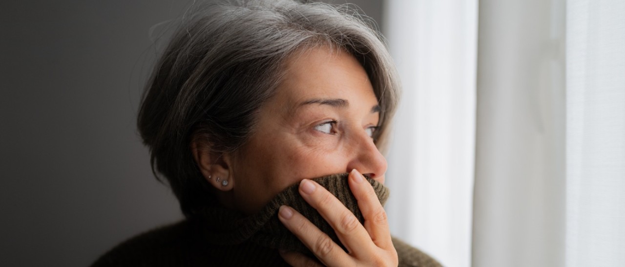 middle-aged woman pulling her sweater over her mouth and looking concerned inside her house