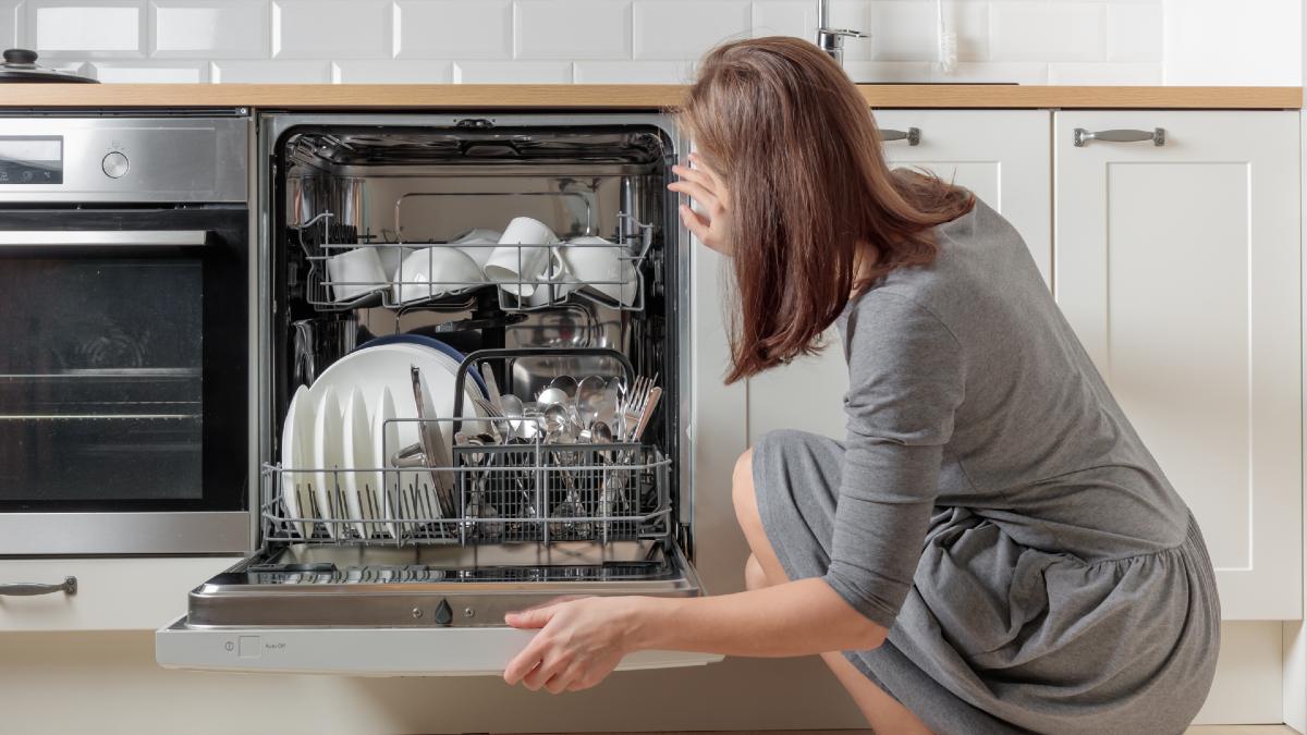 woman crouching in kitchen looking into open dishwasher