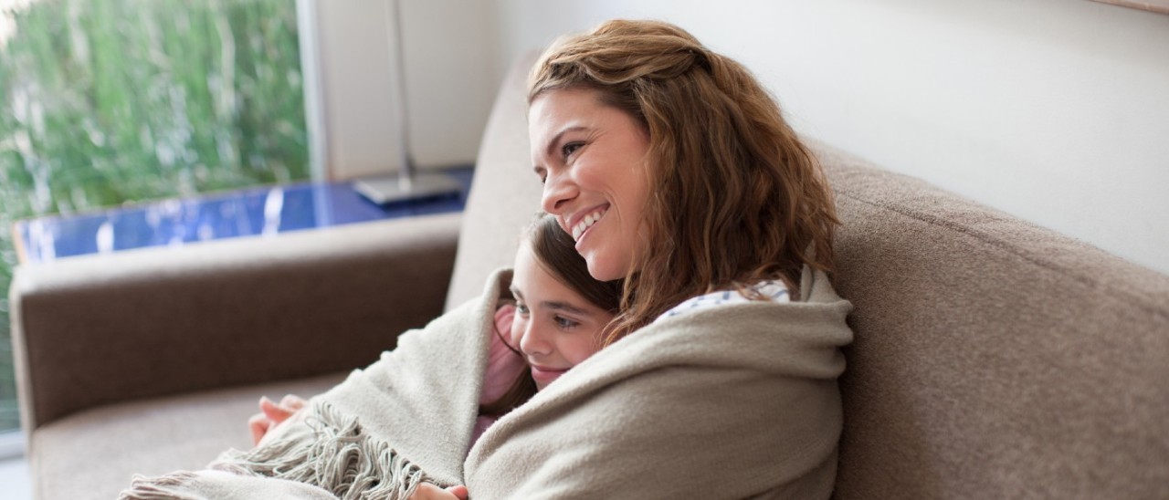 mother and daughter wrapped in a blanket on the couch