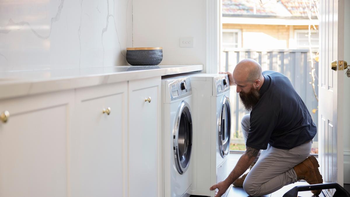 A man with a large beard and bald head installing a washer and dryer in a laundry