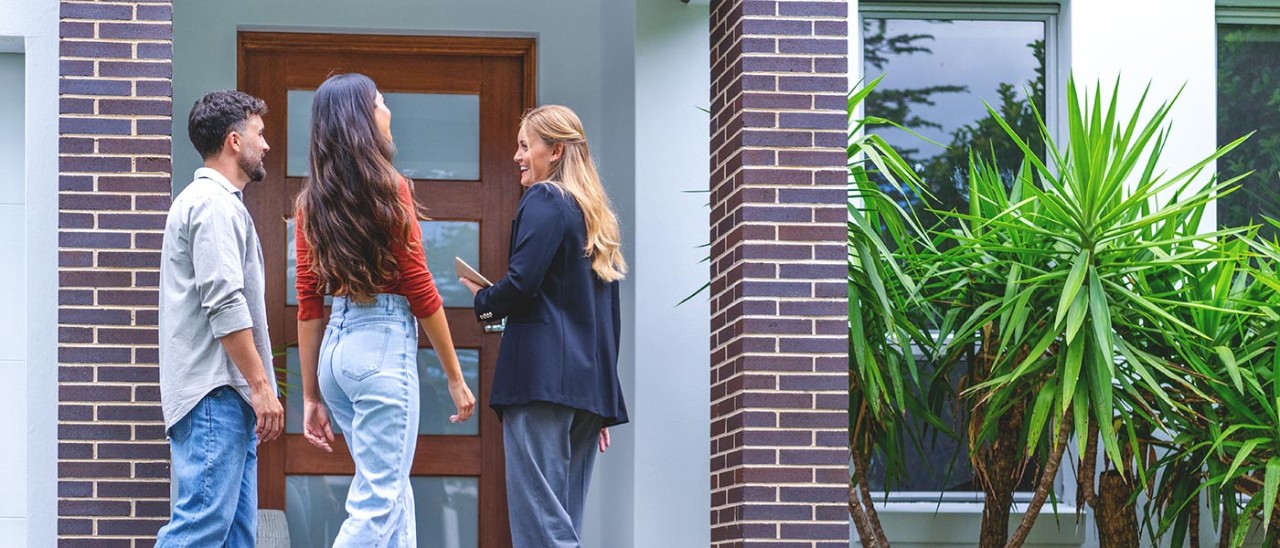 Couple with agent outside new home.
