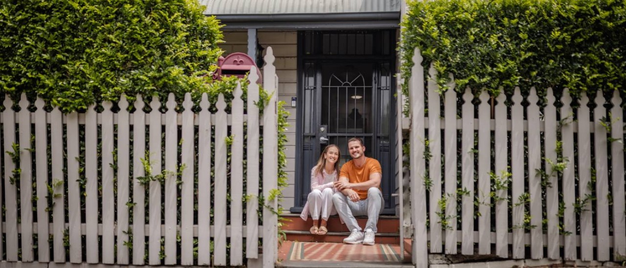 young couple sitting outside their home