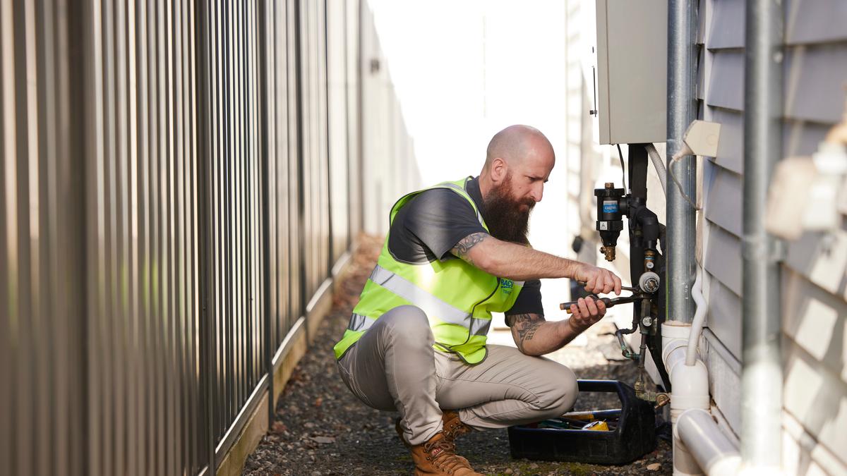 A tradesperson servicing a hot water system outside