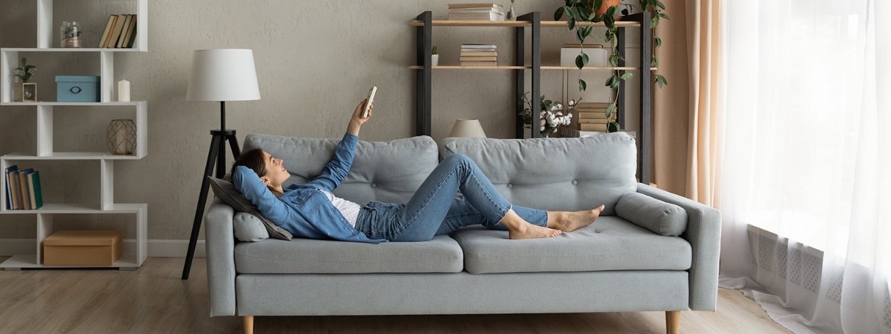 1304127544 woman laying on sofa using aircon remote