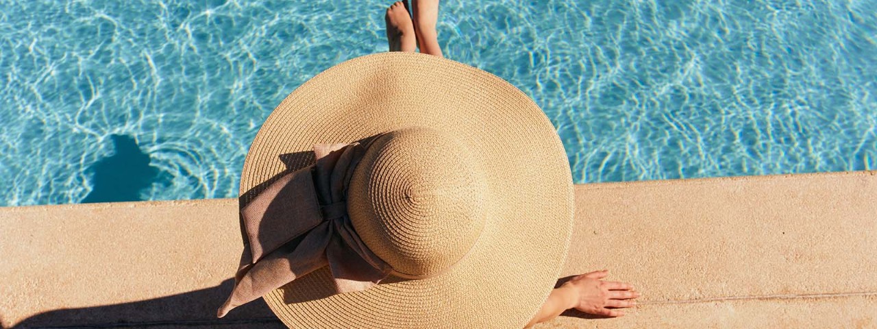 Woman wearing wide brimmed hat sitting beside pool