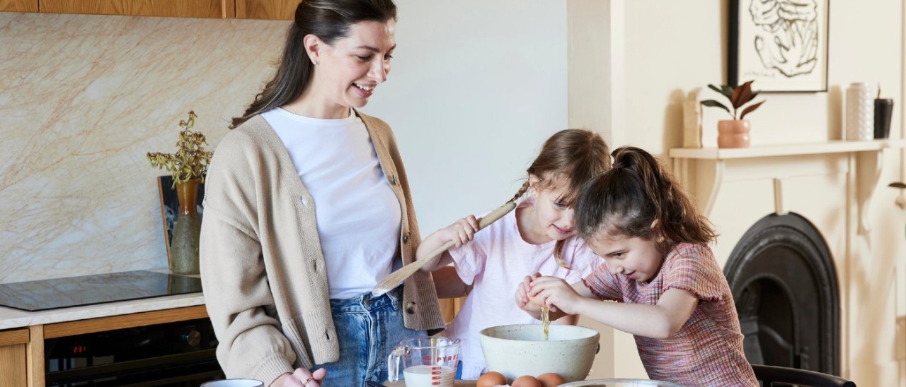 A family cooking A mother and her two young daughters happily cooking at kitchen table. An induction cooktop can be seen in the background.