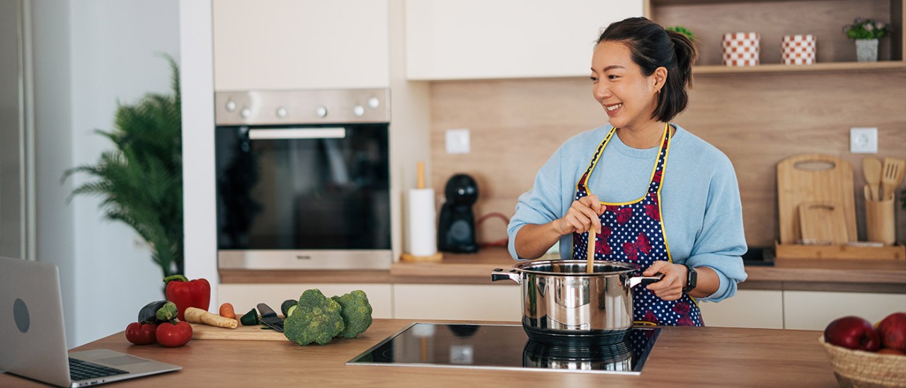 Woman in modern kitchen cooking on induction stovetop.